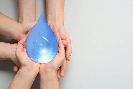 People holding paper water drop on light gray background, top view. Space for textの写真素材