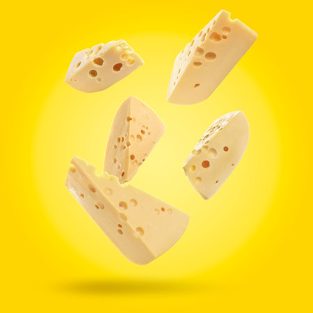 Pieces of delicious cheese falling on yellow backgroundの写真素材