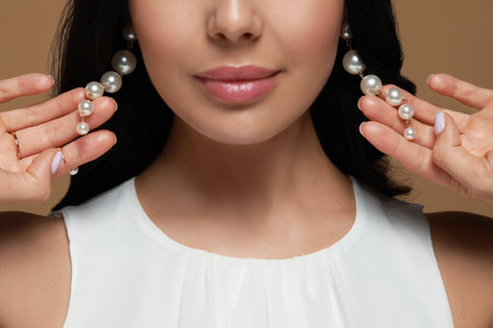 Young woman wearing elegant pearl earrings on brown background, closeupの写真素材