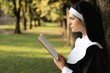 Young nun reading Bible in park on sunny day, space for textの写真素材