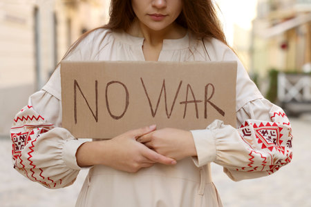 Sad woman in embroidered dress holding poster No War on city street, closeupの写真素材