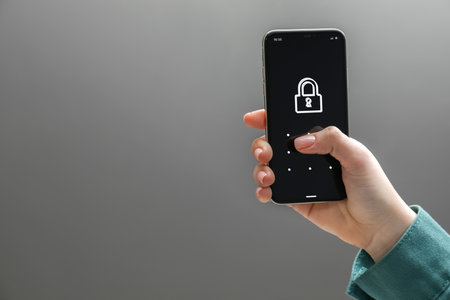 Woman unlocking smartphone with blocked screen on gray background, closeup. Space for text