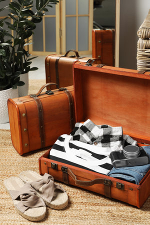 Open suitcase with folded clothes, accessories and shoes on floor in roomの写真素材