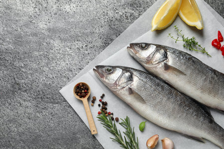 Sea bass fish and ingredients on gray table, above view. Space for text