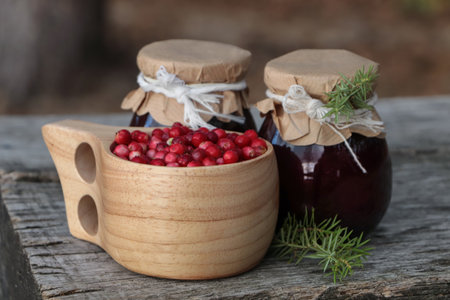 Tasty lingonberry jam in jars and cup with red berries on wooden table outdoorsの写真素材