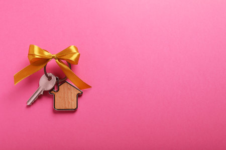 Key with trinket in shape of house and bow on pink background, top view. Space for text. house warming partyの写真素材