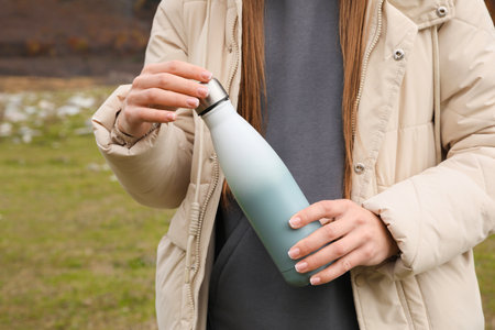 Woman holding thermo bottle in mountains, closeupの写真素材