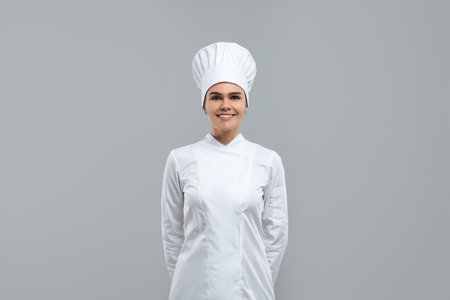 Happy female chef wearing uniform and cap on light gray backgroundの写真素材