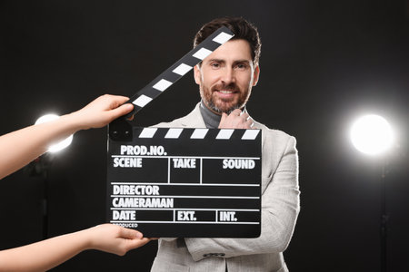 Actor performing while second assistant camera holding clapperboard on black backgroundの写真素材