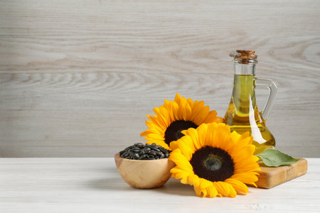 Sunflower cooking oil, seeds and yellow flowers on white wooden table, space for textの写真素材