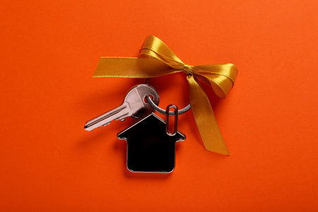 Key with trinket in shape of house and yellow bow on orange background, top view. house warming partyの写真素材