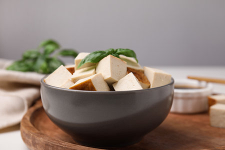 Bowl of smoked tofu cubes and basil on wooden tray, closeupの写真素材