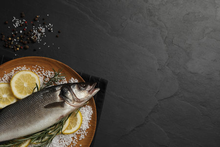Sea bass fish and ingredients on black table, flat lay. Space for textの写真素材