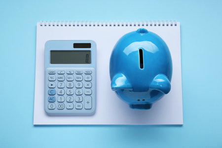 Piggy bank, notebook and calculator on light blue background, top viewの写真素材