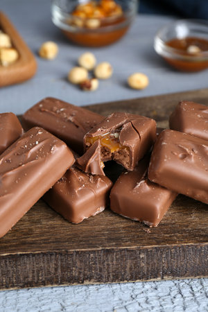 Delicious chocolate candy bars with caramel and nuts on gray wooden table
