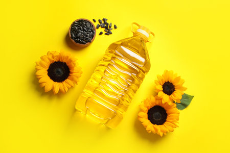 Bottle of cooking oil, sunflowers and seeds on yellow background, flat layの写真素材