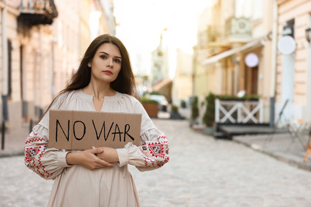 Sad woman in embroidered dress holding poster No War on city street. Space for textの写真素材