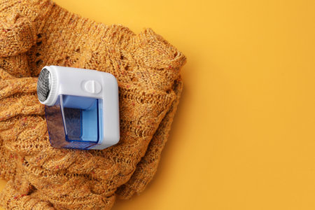 Modern fabric shaver and knitted sweater on orange background, top view. Space for textの写真素材