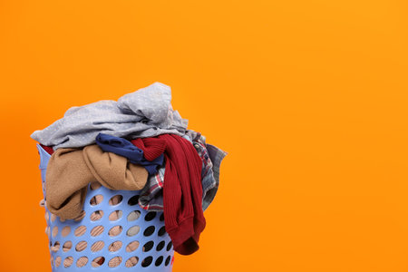 Laundry basket with clothes against orange background. Space for textの写真素材