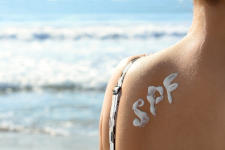 Woman with sun protection cream on her back at beach, closeup. Space for textの写真素材