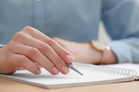 Woman writing in notebook at wooden table, closeupの写真素材