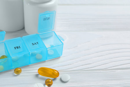 Weekly pill box with medicines on white wooden table, closeup. Space for textの写真素材