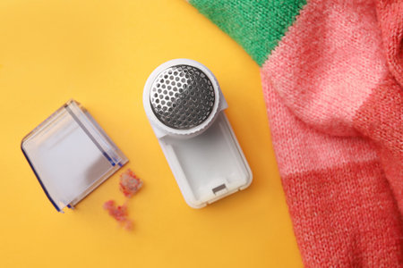Modern fabric shaver and colorful knitted sweater on yellow background, flat layの写真素材