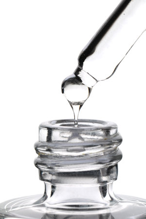 Dripping clear facial serum from pipette into glass bottle on white background, closeupの写真素材