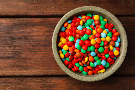 Bowl with tasty colorful candies on wooden table, top view. Space for textの写真素材