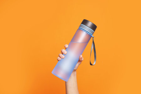 Woman holding bottle of water on orange background, closeupの写真素材