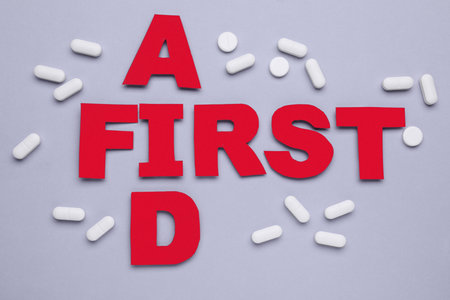 Words First Aid made of red letters and pills on gray background, flat layの写真素材