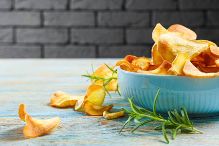 Bowl of tasty homemade parsnip chips and rosemary on old light blue wooden table. Space for textの写真素材