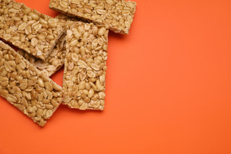 Tasty peanut bars (kozinaki) on orange background, flat lay. Space for text
