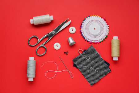 Flat lay composition with thimble and different sewing tools on red background