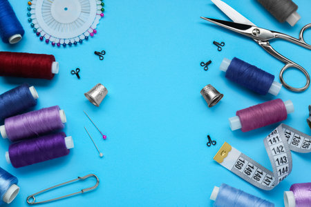 Flat lay composition with thimbles and different sewing tools on light blue background. Space for...