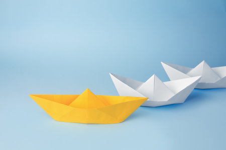 Group of paper boats following yellow one on light blue background. leadership conceptの写真素材