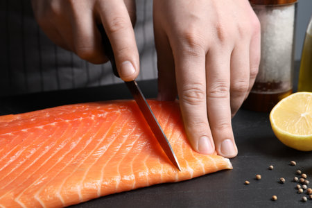 Man cutting raw salmon at black table, closeupの写真素材