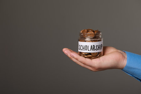 Man holding glass jar with coins against gray background, closeup and space for text. Scholarship conceptの写真素材