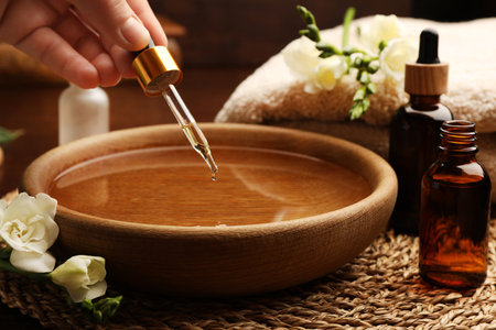 Woman dripping essential oil into bowl at table, closeup. Aromatherapy treatmentsの写真素材