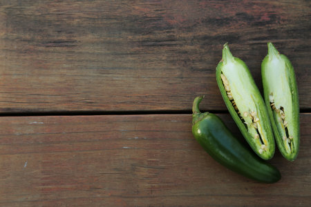 Whole and cut green chili peppers on wooden table, flat lay. Space for textの写真素材
