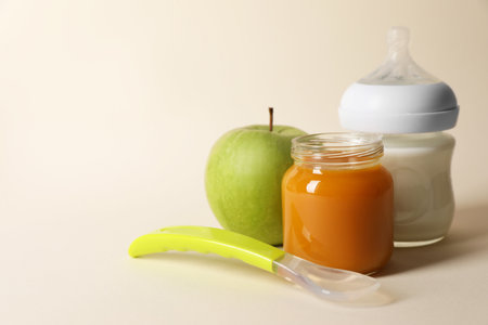 Healthy baby food in jar, bottle of milk, apple and spoon on beige background. Space for textの写真素材