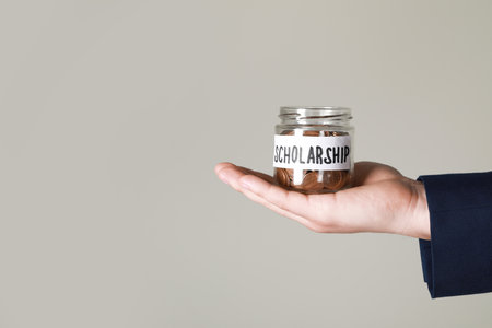 Man holding glass jar with coins against gray background, closeup and space for text. Scholarship...