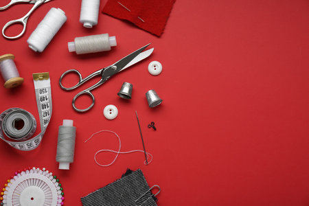 Flat lay composition with thimbles and different sewing tools on red background. Space for textの写真素材