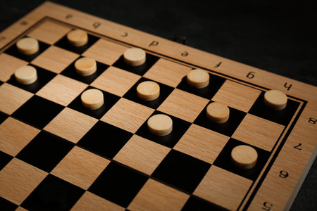 Wooden checkerboard with game pieces on black table, closeup