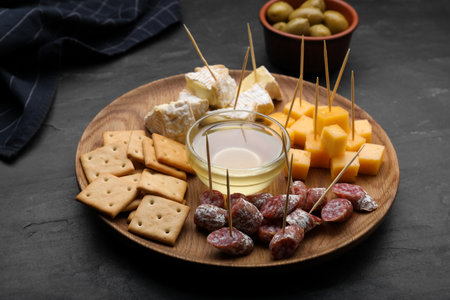 Toothpick appetizers. Pieces of sausage, crackers and honey on black tableの写真素材