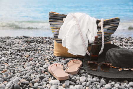 Beautiful hat with sunglasses, bag and flip flops near sea on pebble beachの写真素材