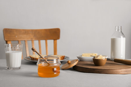 Jar with honey, milk, butter and bread served for breakfast on gray tableの写真素材