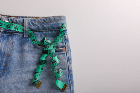Jeans with measuring tape on light gray background, top view and space for text. weight loss conceptの写真素材
