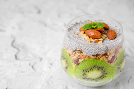 Delicious dessert with kiwi, chia seeds and almonds on light textured table, space for textの写真素材