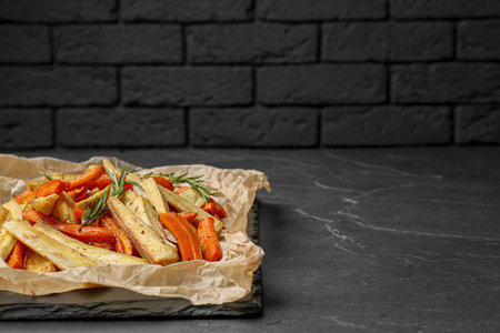 Parchment with tasty baked parsnip and bell pepper on dark gray table, space for textの写真素材
